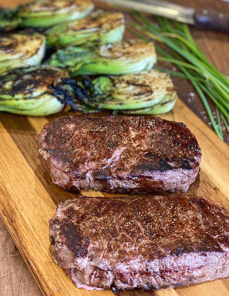 grilled New York strip steak on a cutting board with grilled bok choy