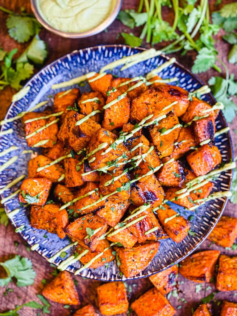 roasted sweet potatoes on a blue plate with avocado cream drizzle