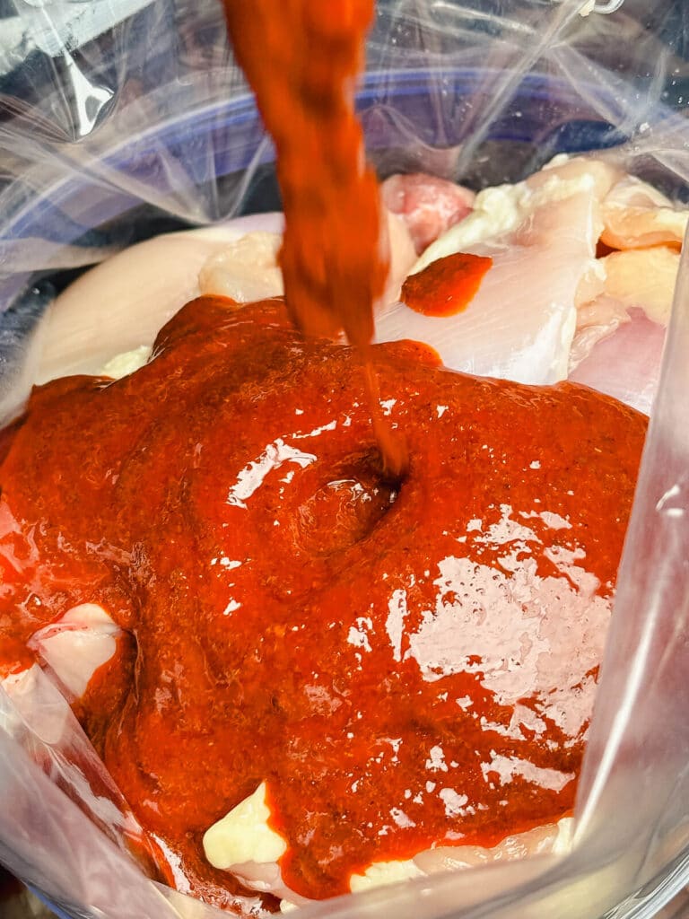 chipotle marinade being poured over chicken thighs in a plastic bag 