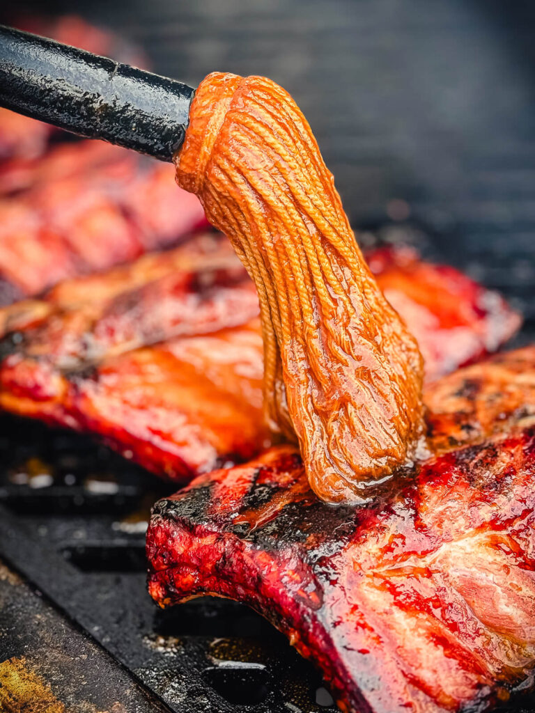 mop sauce being applied to baby back ribs on a grill