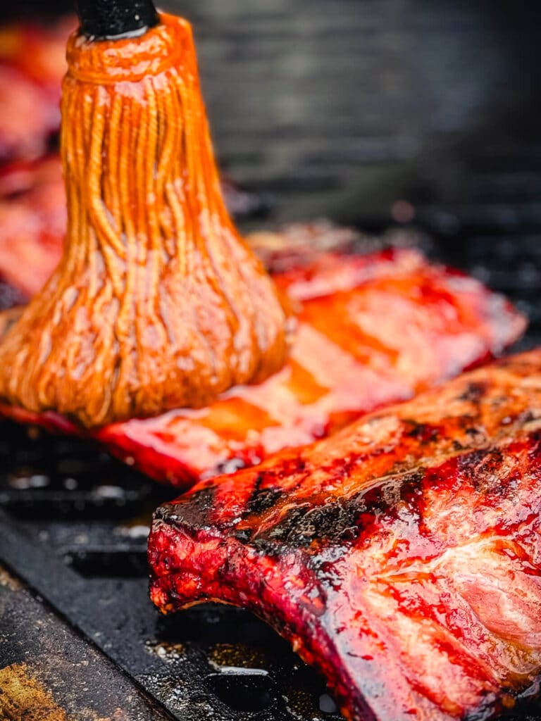 bbq mop with sauce being applied to baby back ribs