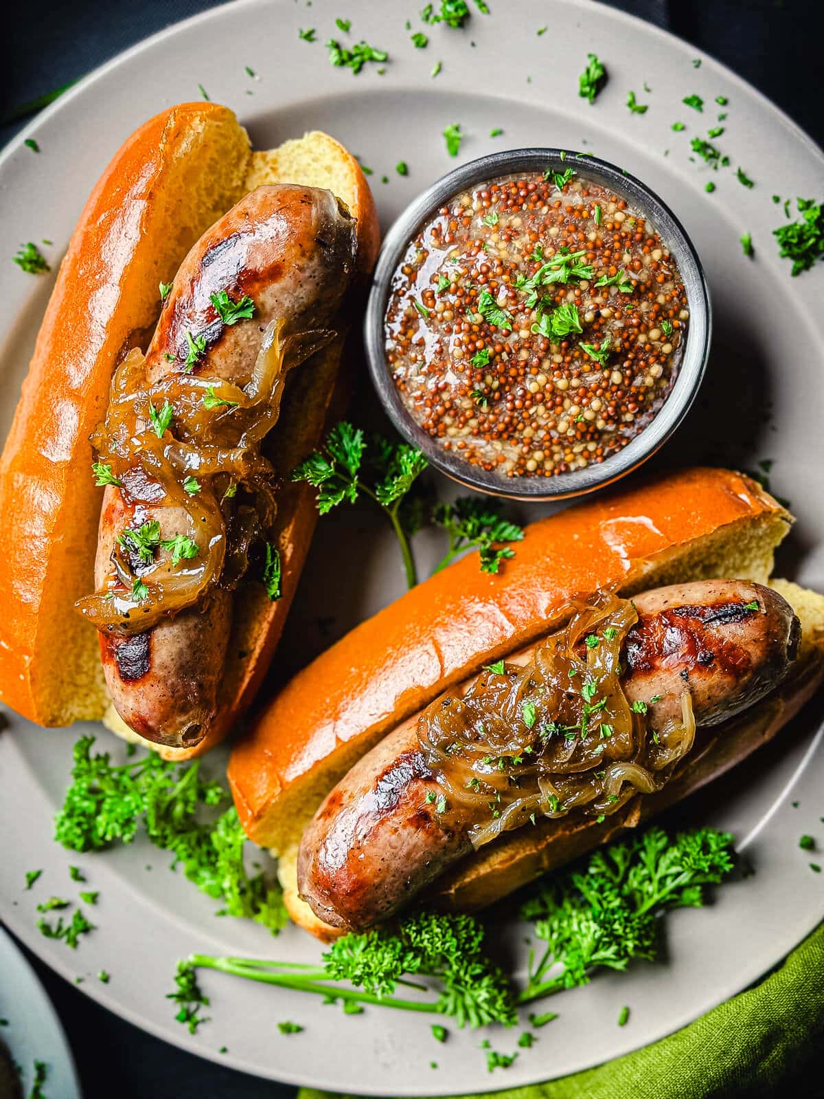 Beer brats in buns on a grey plate with whole grain mustard