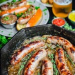 beer brats in a cast iron pan with brats in buns in the background