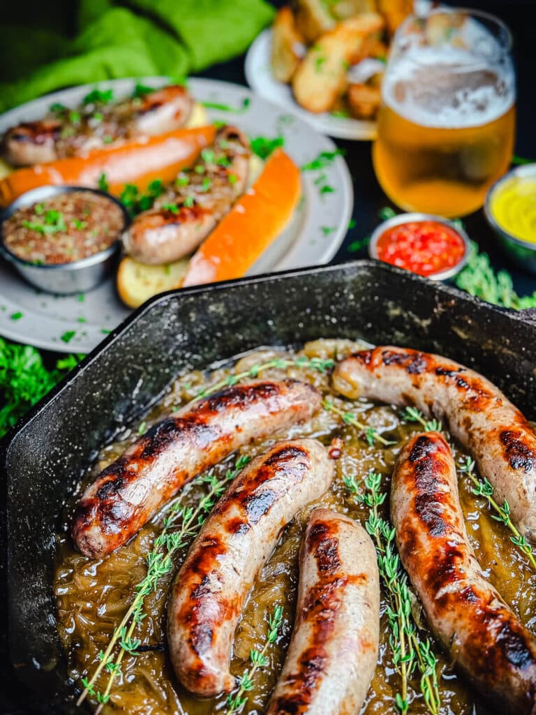 beer brats in a cast iron pan with brats in buns in the background