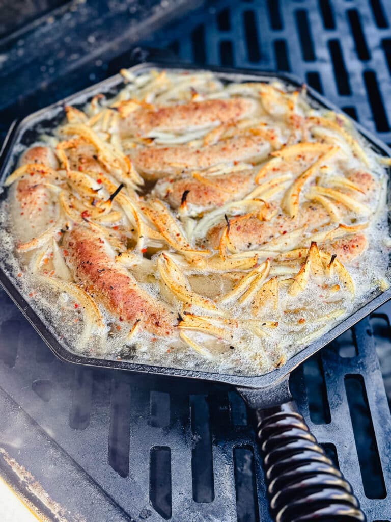 beer brats in a cast iron pan on the grill