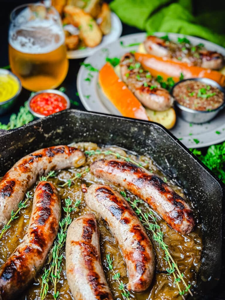 beer brats in a pan with some in a bun in the background