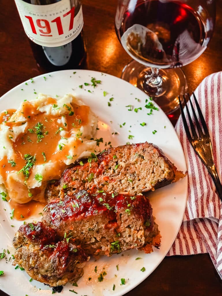 slices of meatloaf on a plate with mashed potatoes and wine