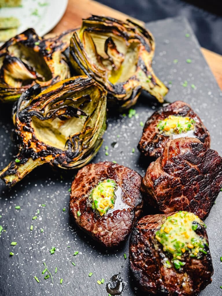 grilled artichokes and ribeye steaks on a cutting board