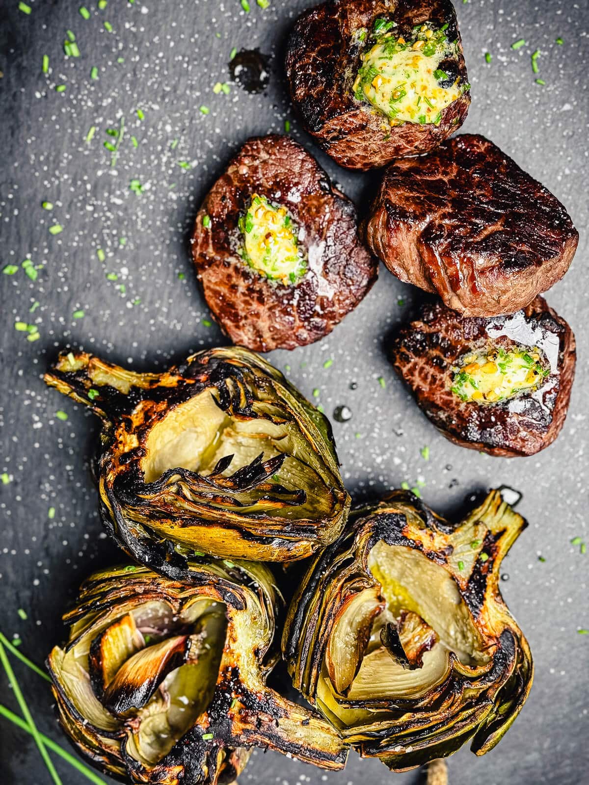 grilled ribeye steaks and artichokes on a cutting board