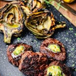 grilled ribeye steaks with pistachio butter on a black cutting board