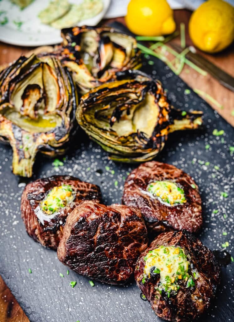 grilled ribeye steaks with pistachio butter on a black cutting board