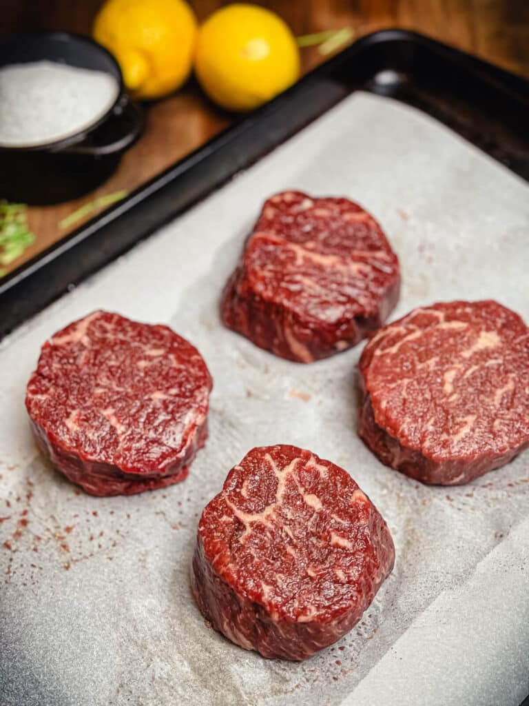 raw ribeye steaks seasoned with kosher salt on a tray