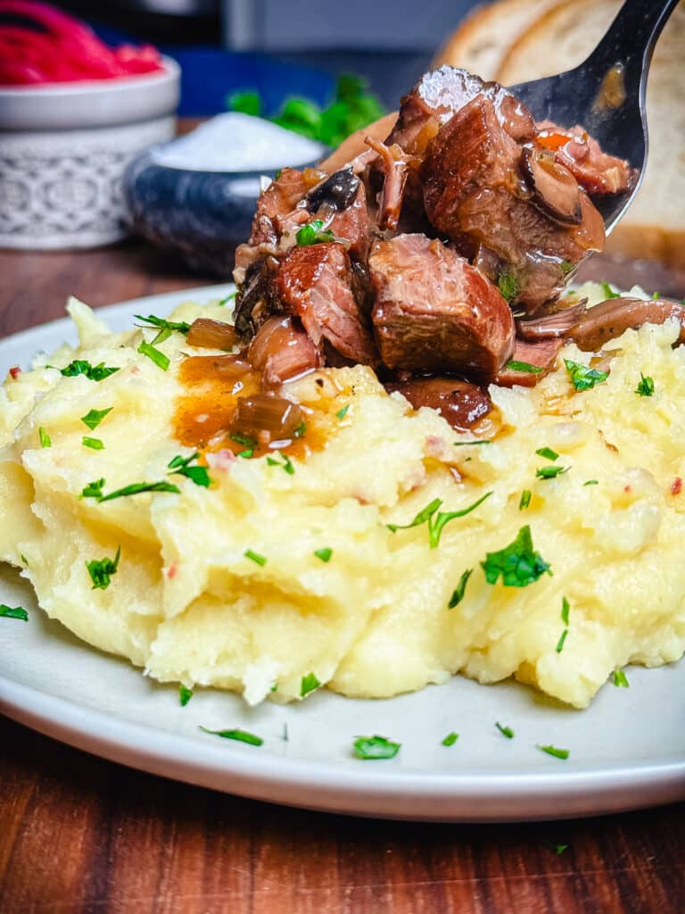 crockpot beef tips being added to mashed potatoes