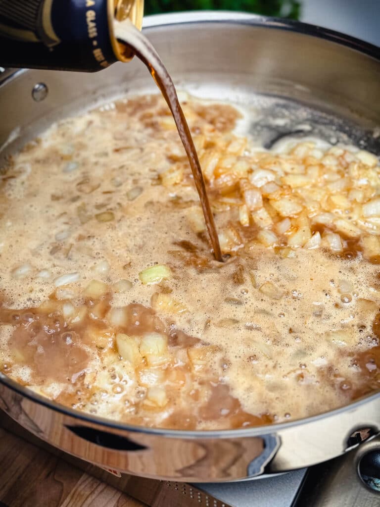 beer being added to cooked onions in a pan