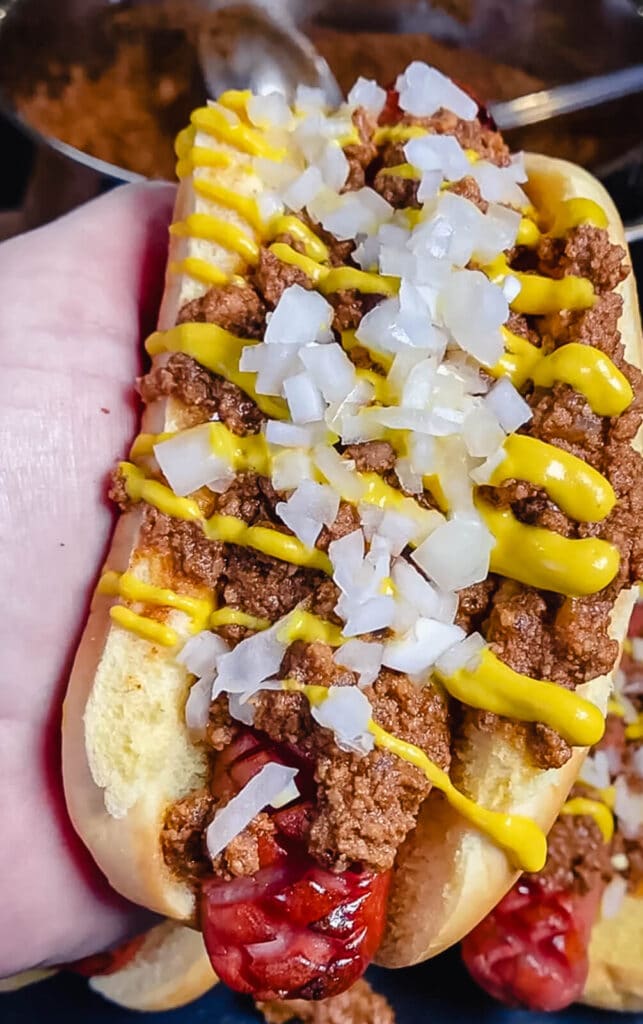 holding a coney island hot dog with mustard and onions