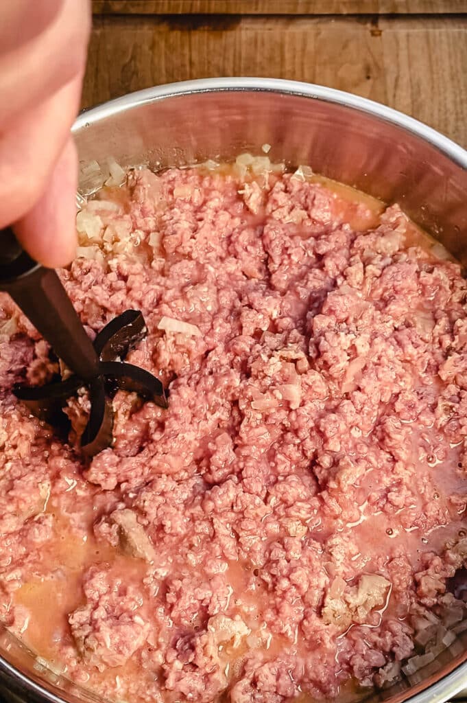 ground beef being broken up by a meat masher