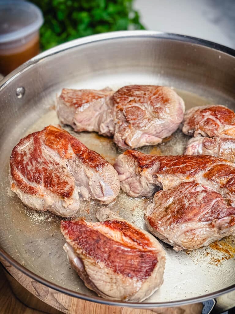 slices of lamb searing in a large pan