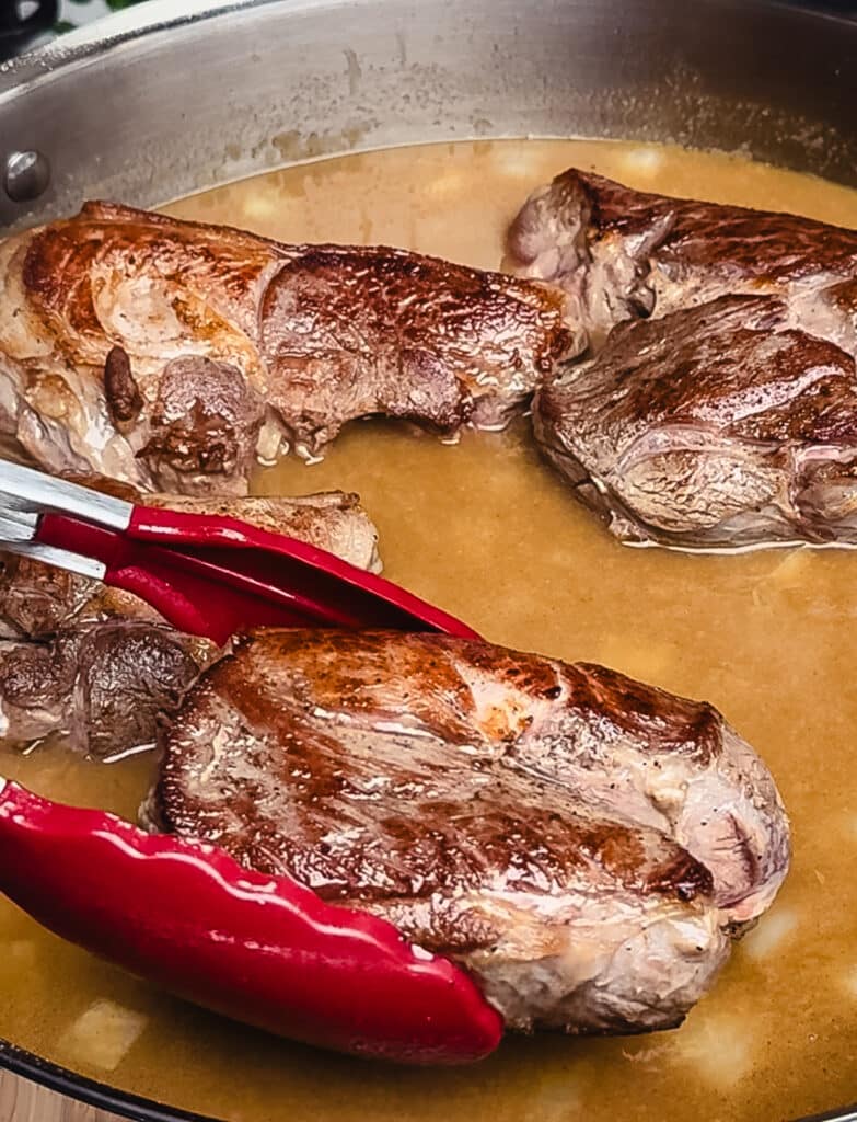 adding lamb to stew with tongs