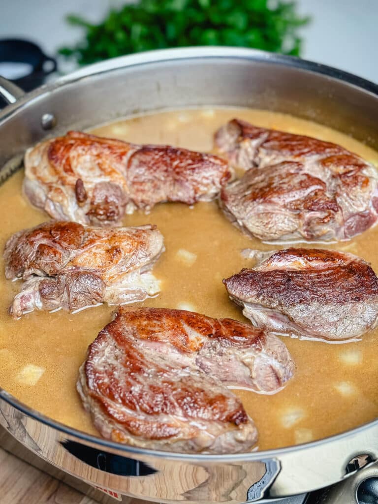 seared lamb added to stew broth in a pan