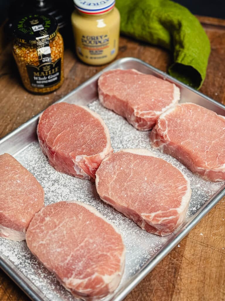 uncooked pork chops with salt on a cooking sheet