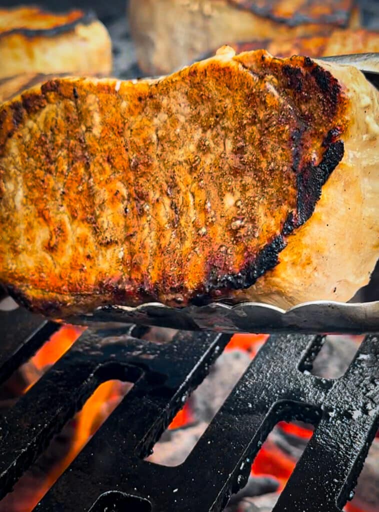 pork chop being flipped over on a hot grill